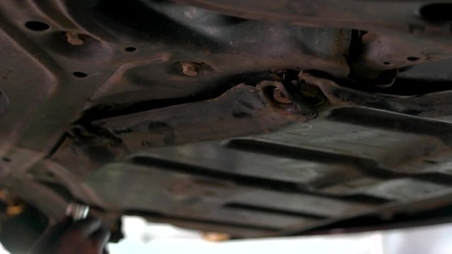 An auto mechanic screws crankcase protection with a pneumatic wrench in the service station. Close-up bottom of lifted car. Dirty hands of mechanic.