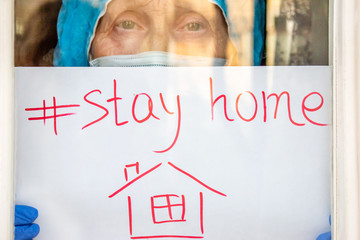 A elderly woman doctor in uniform shows a paper with inscription stay at home holding on hand. Protect from Coronavirus or Covid-19 epidemic. Concept stay home. Doctor's appeal to people. Health