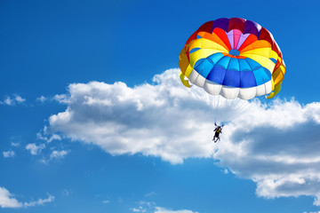 Paragliding using a parachute on the background of cloudy blue sky.