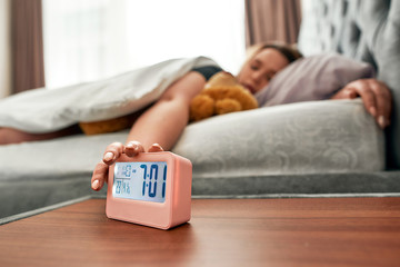 Time to get up. Young woman pressing snooze button on early morning digital alarm clock