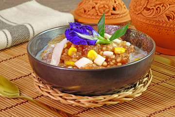 Thai dessert : Sago Pearl with sweet corn , dressing with fresh coconut milk, topping with young coconut meat, decorated with blue pea flower and pandan leaf. Selective focus.