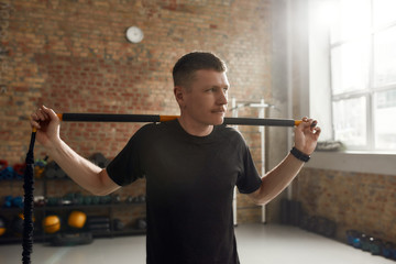 Bring the focus on fitness. Sportive man looking aside, using pilates exercise body stick or bar...