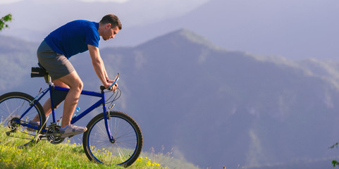 FIt male Cyclist is speeding up his bicycle downhill while enjoying the amazing mountain dirt road.