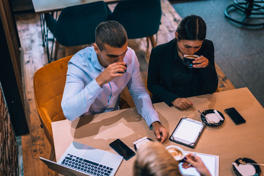 Top view of a beautiful young couple talking to their realtor while using tablet and drinking coffee at table in cafe