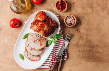 Roasted sliced pork ham on a white plate on a beige rustic background.