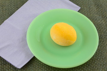 Mango ice cream mochi ball on green dessert plate with lavender napkin