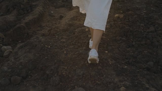 A girl walks along the summer island during sunset. Legs of a girl in beauties and a long white dress walk on mountains, stones. Atmospheric video