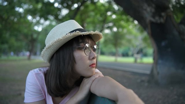 Holiday concept. An Asian girl is sitting lonely on a bench in the garden. 4k Resolution.