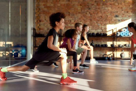 Make your commitment. Portrait of a boy smiling while warming up, exercising together with other kids and female trainer in gym. Sport, healthy lifestyle, physical education concept