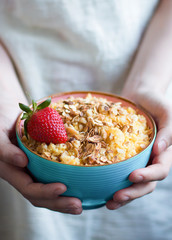 Blue plate of corn porridge with granola and strawberry in the hands of a girl. Healthy, diet, vegan or food concept.