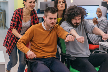 Team building and office fun.Four young cheerful businesspeople in smart casual wear having fun while racing on office chairs and smiling..