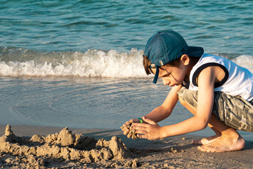 Concentrated boy builds a sand castle on the seashore. Concept for Children's Day with place for...