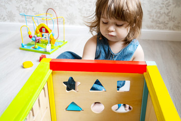 Little cute girl plays a sorter. The baby puts the figure in the hole. early learning concept