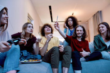  Young guy showing marijuana joint or hashish cigarette to his surprised friends while relaxing together on the coach at home