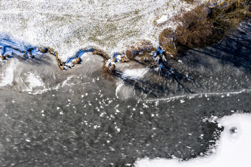 Aerial drone view flying forwards over a frozen lake with trees on the shores