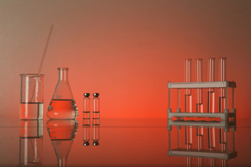 Fototapeta na wymiar chemical flasks and lab glassware with reflection on glass table on red background with copy space.