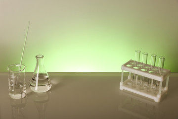 chemical flasks and lab glassware with reflection on glass table on green background with copy space.