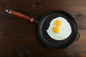 two fried eggs is in the pan on dark wooden background