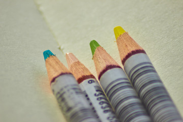 Four colourful pencils on a clean sketchbook page close-up top-view. Pencils for drawing, art and creativity.