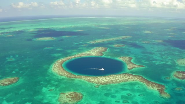 Aerial view of nautical vessel moving on large marine sinkhole, scenic view of seascape while drone moving backward - Great Blue Hole, Belize