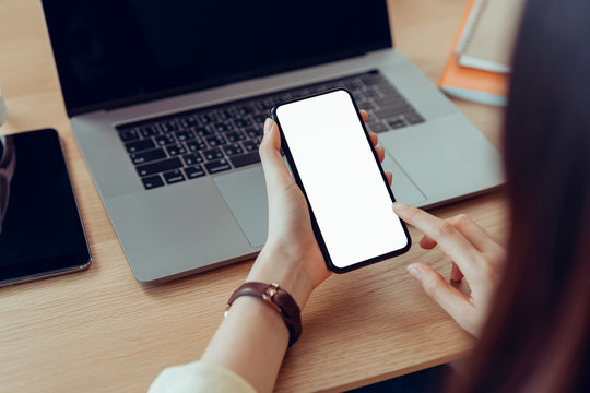 Woman hand holding smartphone with blank copy space screen for your advertisement. laptop on the table.
