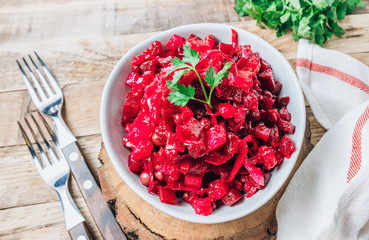 Russian traditional beetroot salad with beetroot, potato, carrot, cucumber, pea and oil dressing. Beet salad on a bowl over wooden background.
