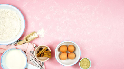 Baking flatlay creative composition top view for basic recipes including eggs, flour, milk and vanila spices, with cooking accessories on modern textured pink background table. Negative copy space.