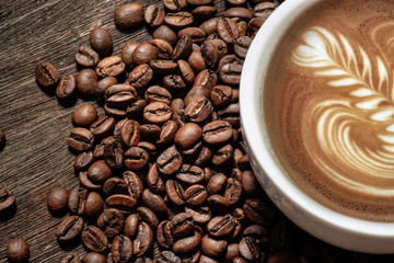 Latte hot coffee in a white cup with latte art and roasted coffee beans on wooden table background