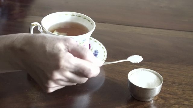 Woman hand putting some granulated sugar in cup of tea and stirs.