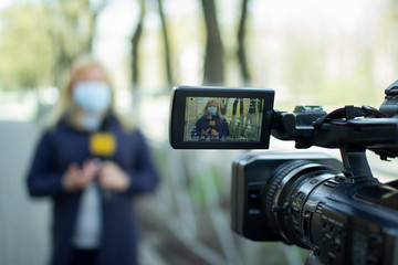 A female journalist in a protective medical mask is reporting in a deserted city. Concept of...