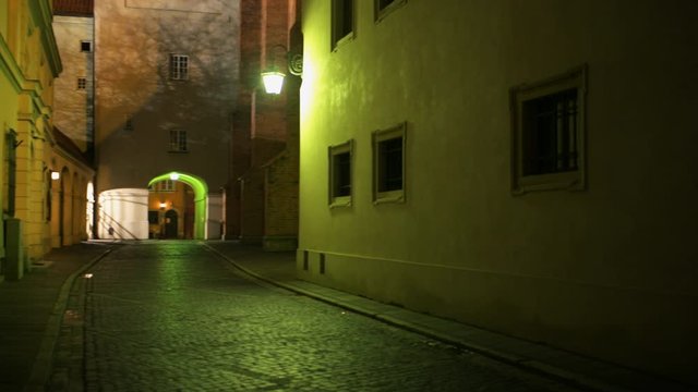Warsaw, Poland - December 24, 2019: Old town back alley narrow empty street at night handheld pov walking panning looking up on church exterior with green lamp