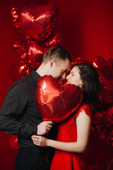 Loving couple with red balloons hearts. Man and woman celebrate valentine's day. Romantic date on a red background. Boyfriend and girl have fun on holiday.