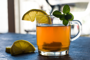 A horizontal view of cup with ginger tea and lemon on a rustic blue table.