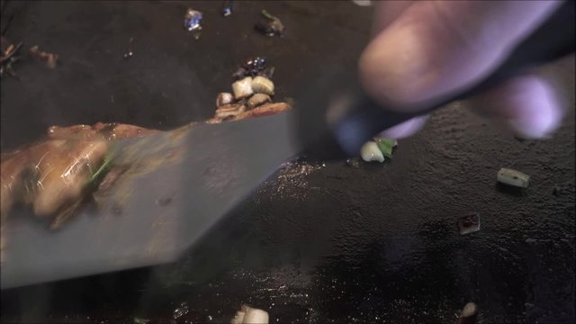 Glazing chicken meat on black gridle with green spring onions.