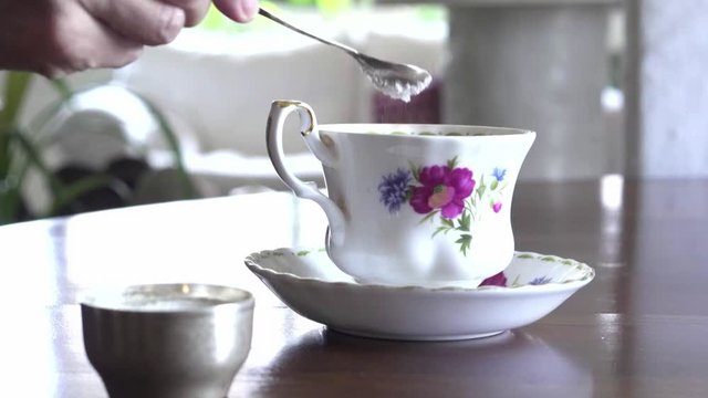Female puts some sugar in her cup of tea with a silver spoon.