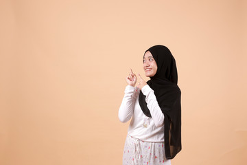 Portrait of young Asian Muslim happy woman smiling and pointing to presenting something on her side, with copy space. Indonesian woman