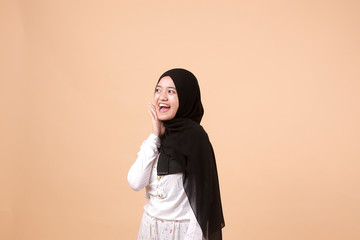 Portrait of happy young Muslim Asian Girl laughing hard with big open mouth, over orange background. Indonesian woman