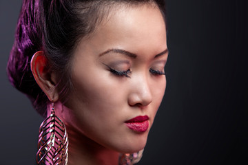 portrait of a beautiful asian woman with gold earrings and red lips being happy and posing in isolated background. she long black hair and smooth clean skin