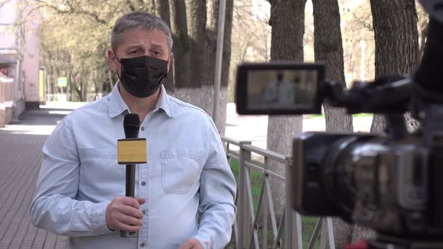A middle- aged European journalist in a protective medical mask is reporting in a deserted city.