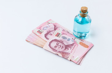Ethanol alcohol in glass bottle with Thai bank note on white background, buy and sale concept, cleaning and hygiene product