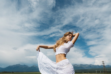 Fototapeta na wymiar Girl in a white dress on a background of mountains and a cloudy sky