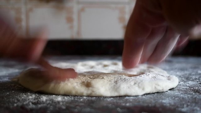 Working on a home made pizza dough with the bare hands on a marble kitchen counter. Natural window light.