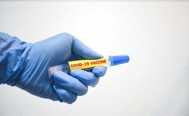 Hand wearing blue rubber nitride glove holding a tube of Coronavirus vaccine.Test tube with covid-19 vaccine word.