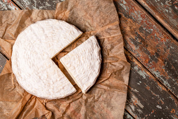 Creamy Brie on kraft paper, rustic wooden background, top view