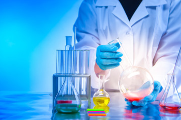 Chemical laboratory. The concept is to conduct chemical experiments. Lab technician's hands with a flask close-up. Chemical dishes and reagents on the table. Analysis of synthetic substances.