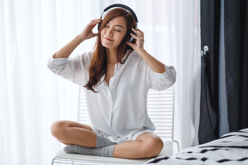 A beautiful asian woman enjoy listening to music with headphone in bedroom , happiness and relaxation concepts