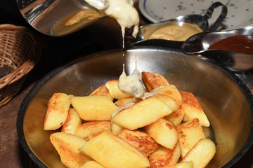 Fried potato dumplings served in a pan with sausages, fried onion, cheese sauce.