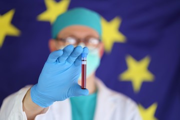 Doctors in the European Union concept.Blood test. Medicine and health in Europe. Doctor in a medical protective mask with a test tube of blood on the background of the flags of Europe.