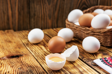Farm eggs white and brown lie on a wooden table and in a basket, close-up, low light, selective focus, shallow depth of field. Organic food concept