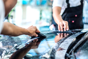 two detailing film paint protection men specialist cleaning and wrapping car in garage showroom,...